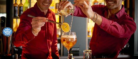 Two individuals preparing a drink at a bar with a beer tap and various bottles in the background.