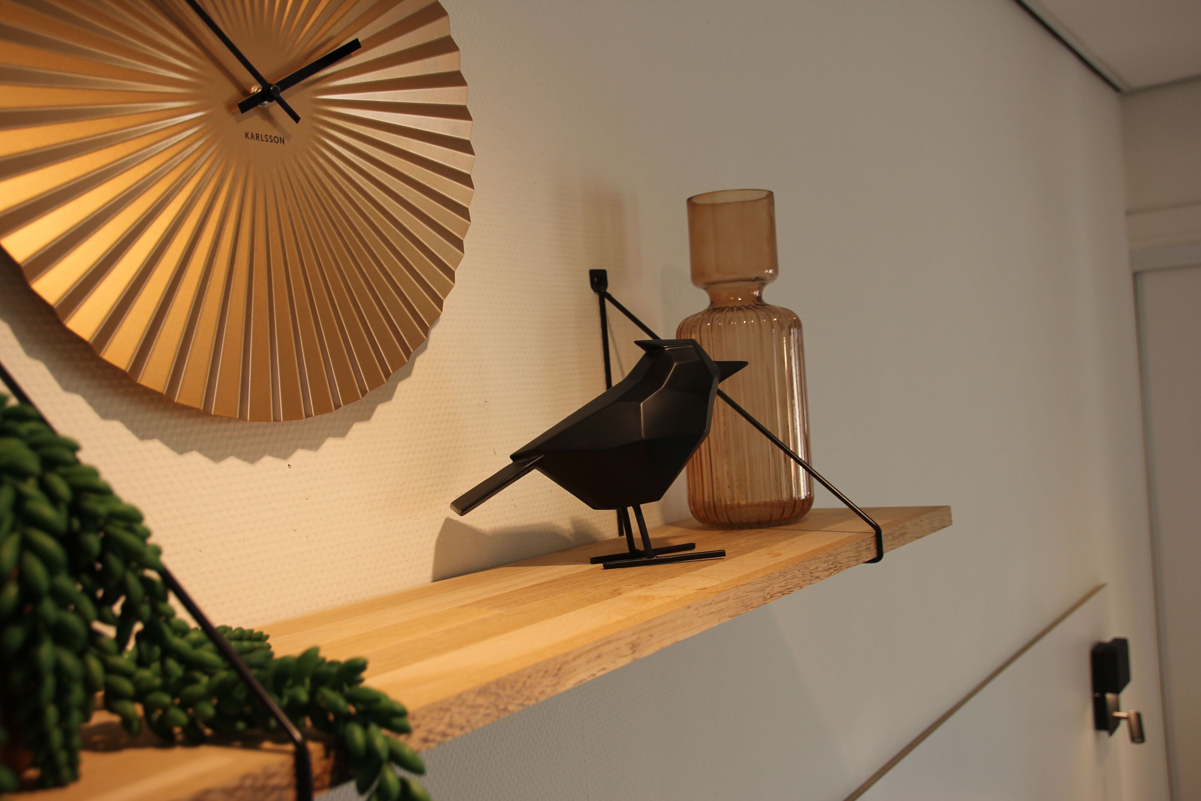 A bird on a wooden shelf, a decorative wall clock, and a vase.