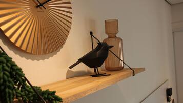 A bird on a wooden shelf, a decorative wall clock, and a vase.
