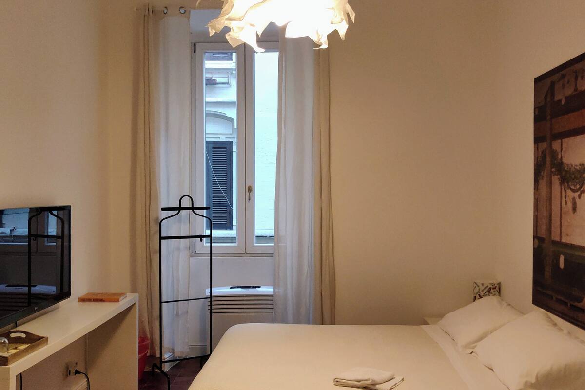 A hotel room with a bed, a TV on a stand, a heater, and a window with curtains.