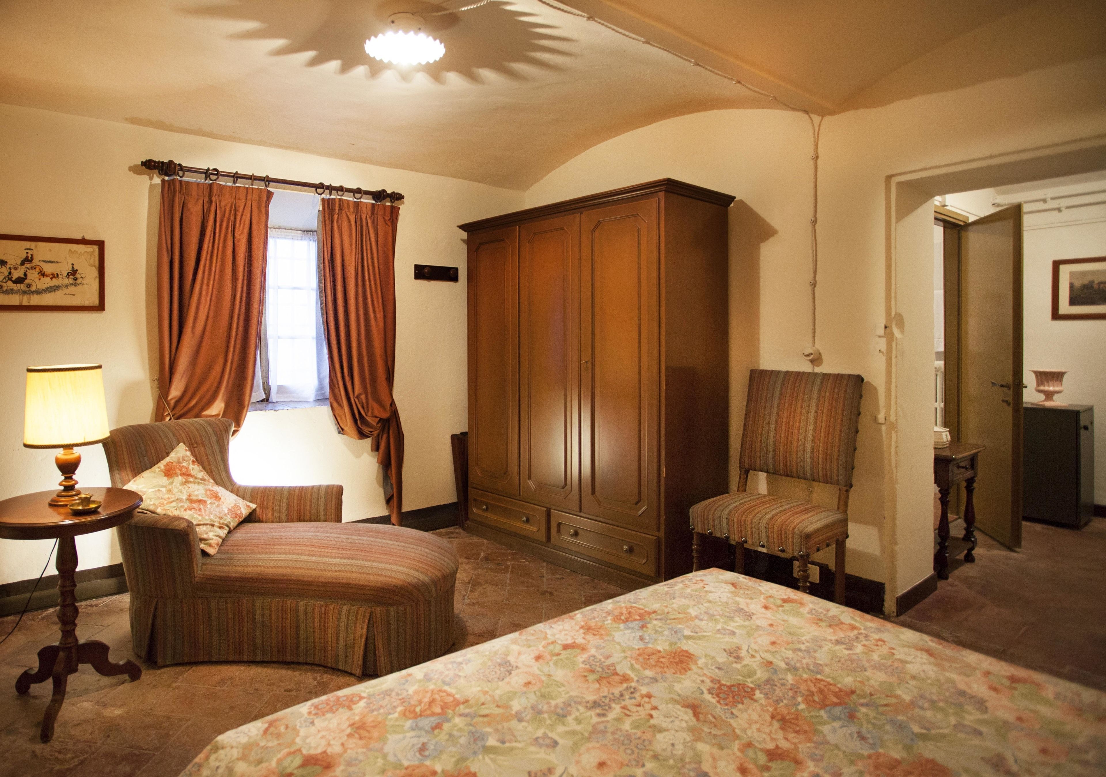Habitación de hotel con cama, dos sillas, armario de madera, lámpara y cortinas.