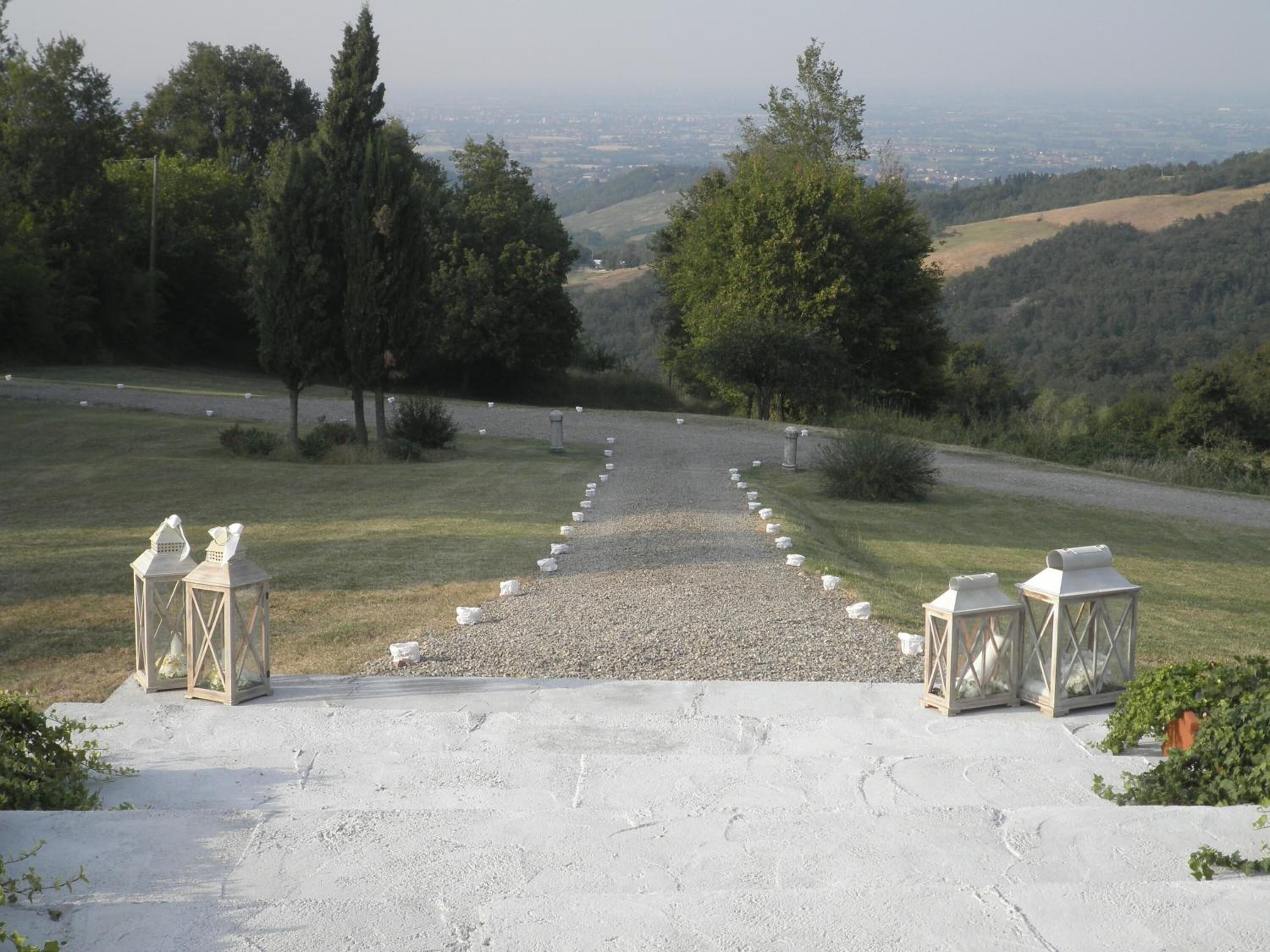 A gravel path leading to a white structure with lanterns, surrounded by trees and a view of distant hills.