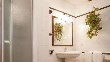 A bathroom with a glass shower enclosure, a sink, a small stool, and a towel rack.