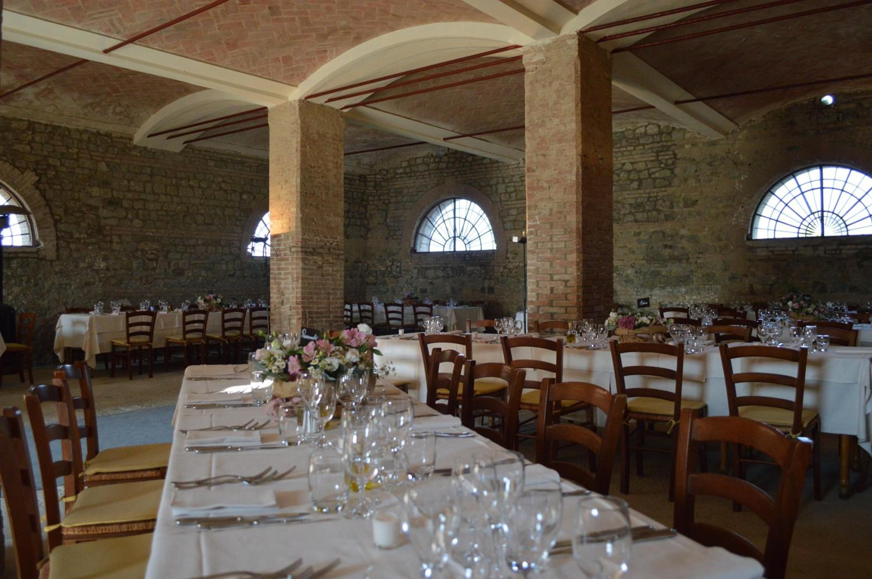 A banquet hall with long tables set for dining, stone walls, and arched windows.