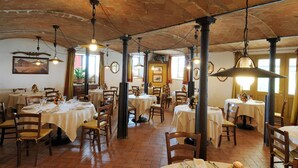 A restaurant with brick ceiling, wooden tables, and hanging pendant lights. - Cavazzone (Viano)