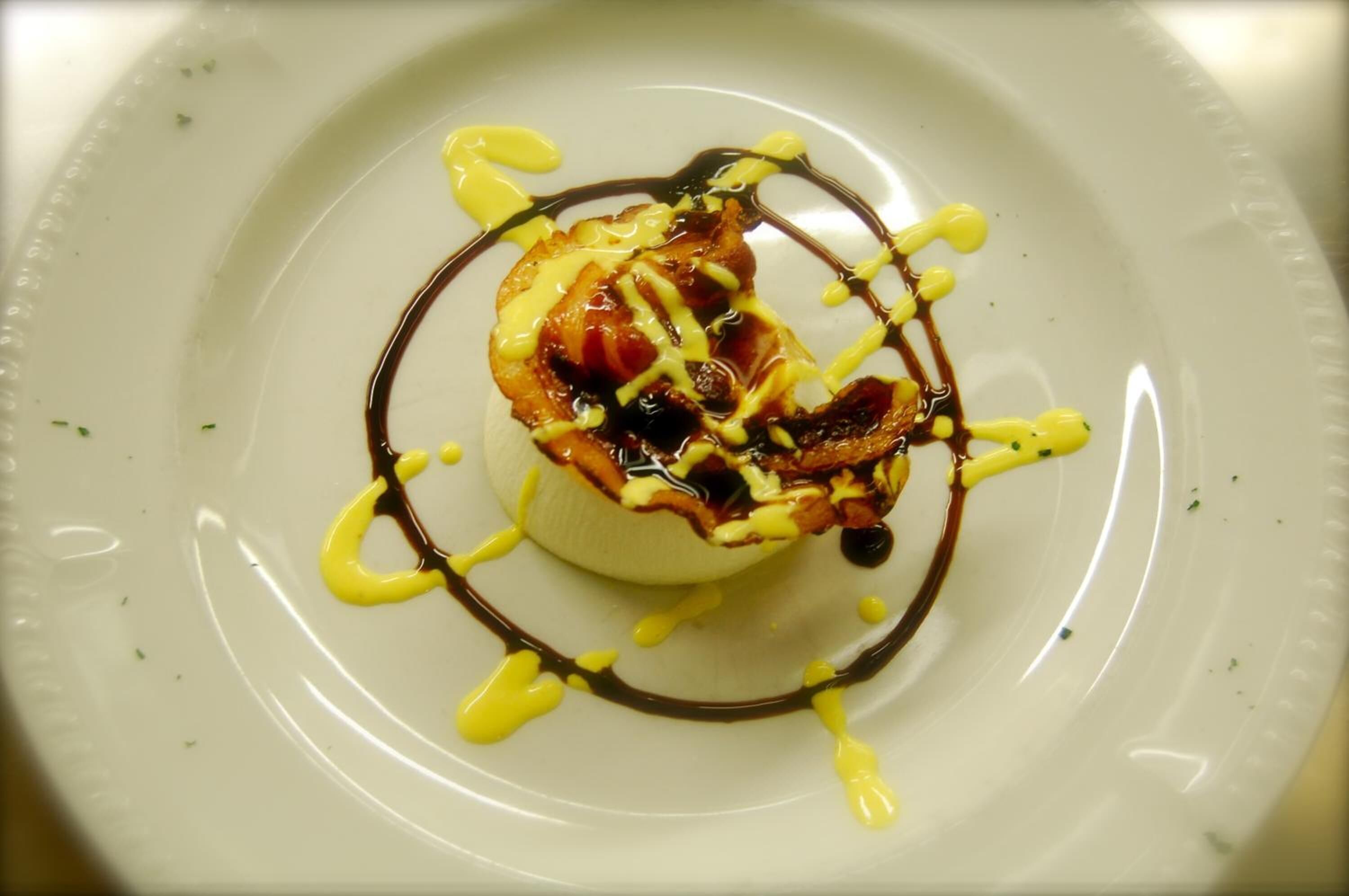 Un dessert servi dans une assiette blanche, nappé de sauce au chocolat et de sauce jaune.