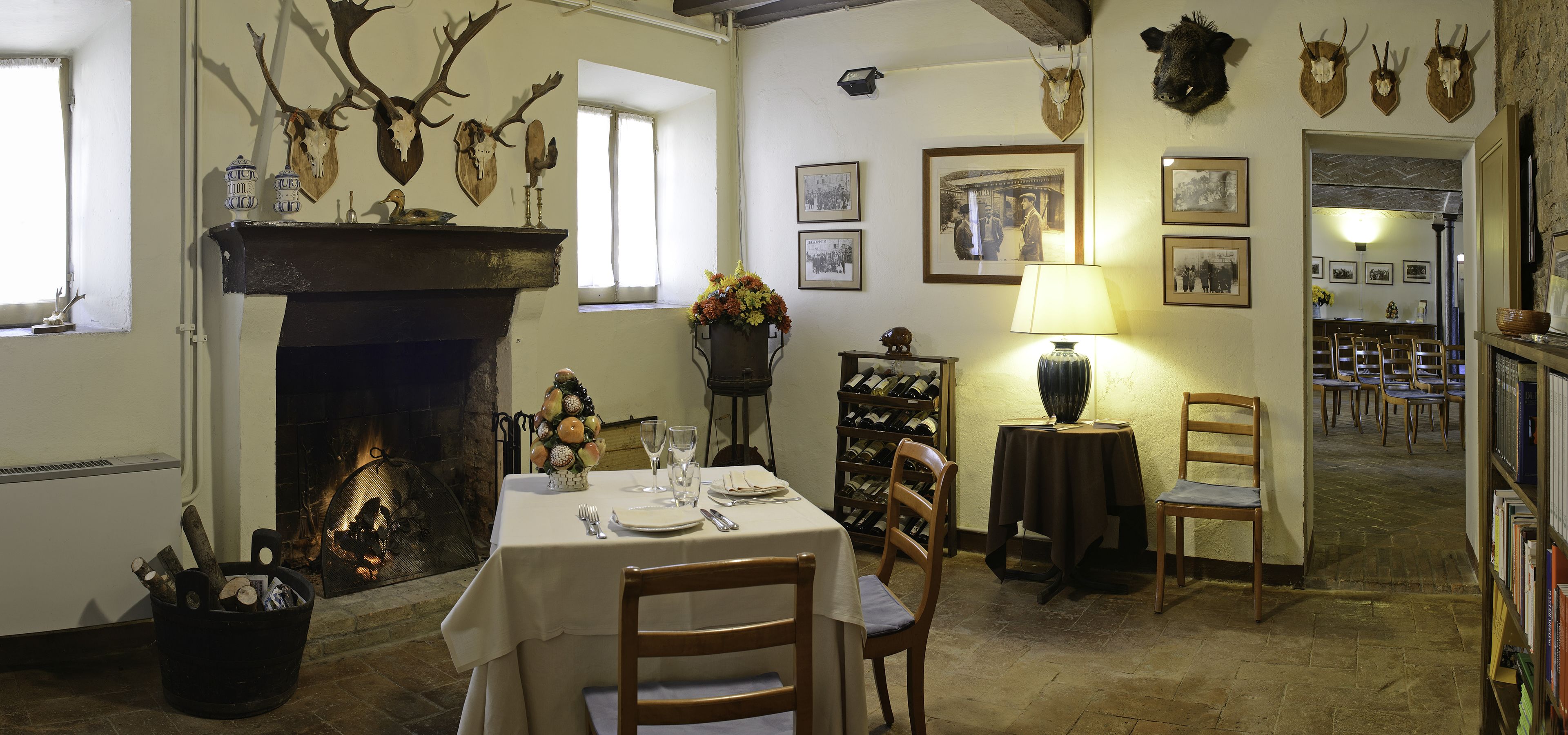 Un coin repas avec une cheminée, des chaises en bois, une table dressée pour deux personnes et un meuble à vin.