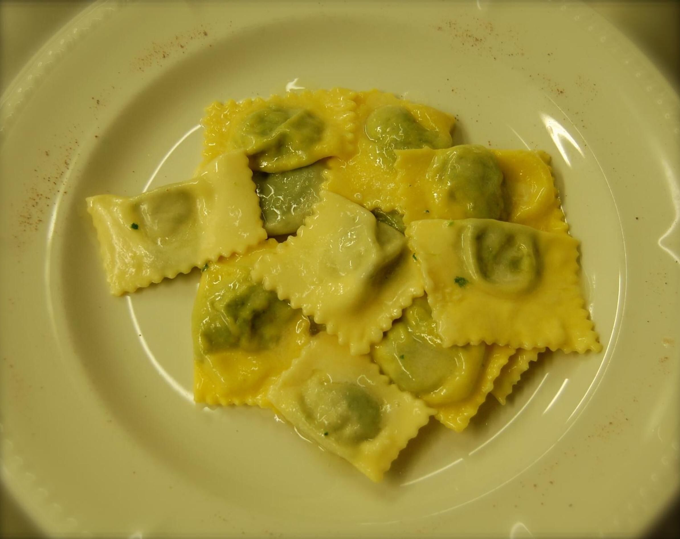 A plate of ravioli with a yellow sauce and green filling.