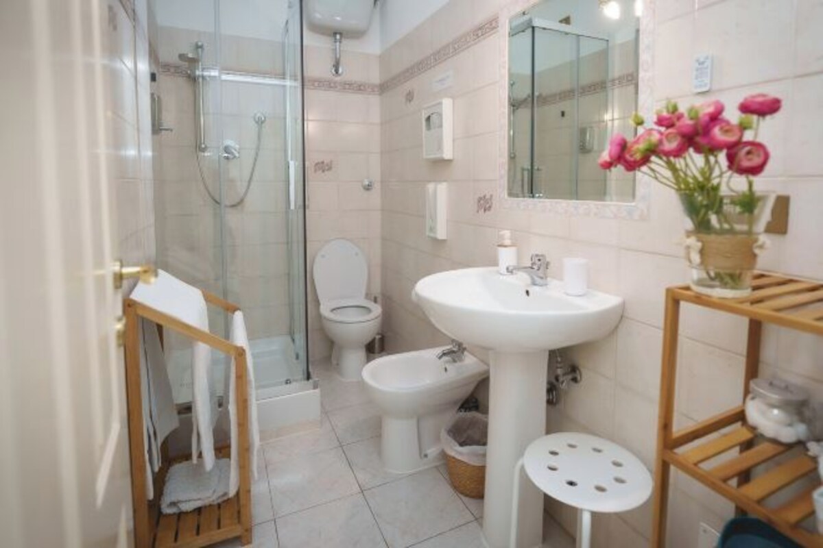 A bathroom with a glass shower enclosure, a toilet, a bidet, a sink, and a mirror.