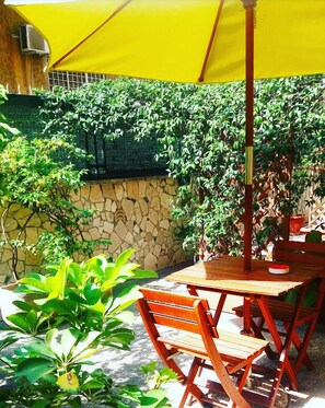 An outdoor patio with a table and chairs, a yellow umbrella, and lush greenery. - Le Tare (Rome)
