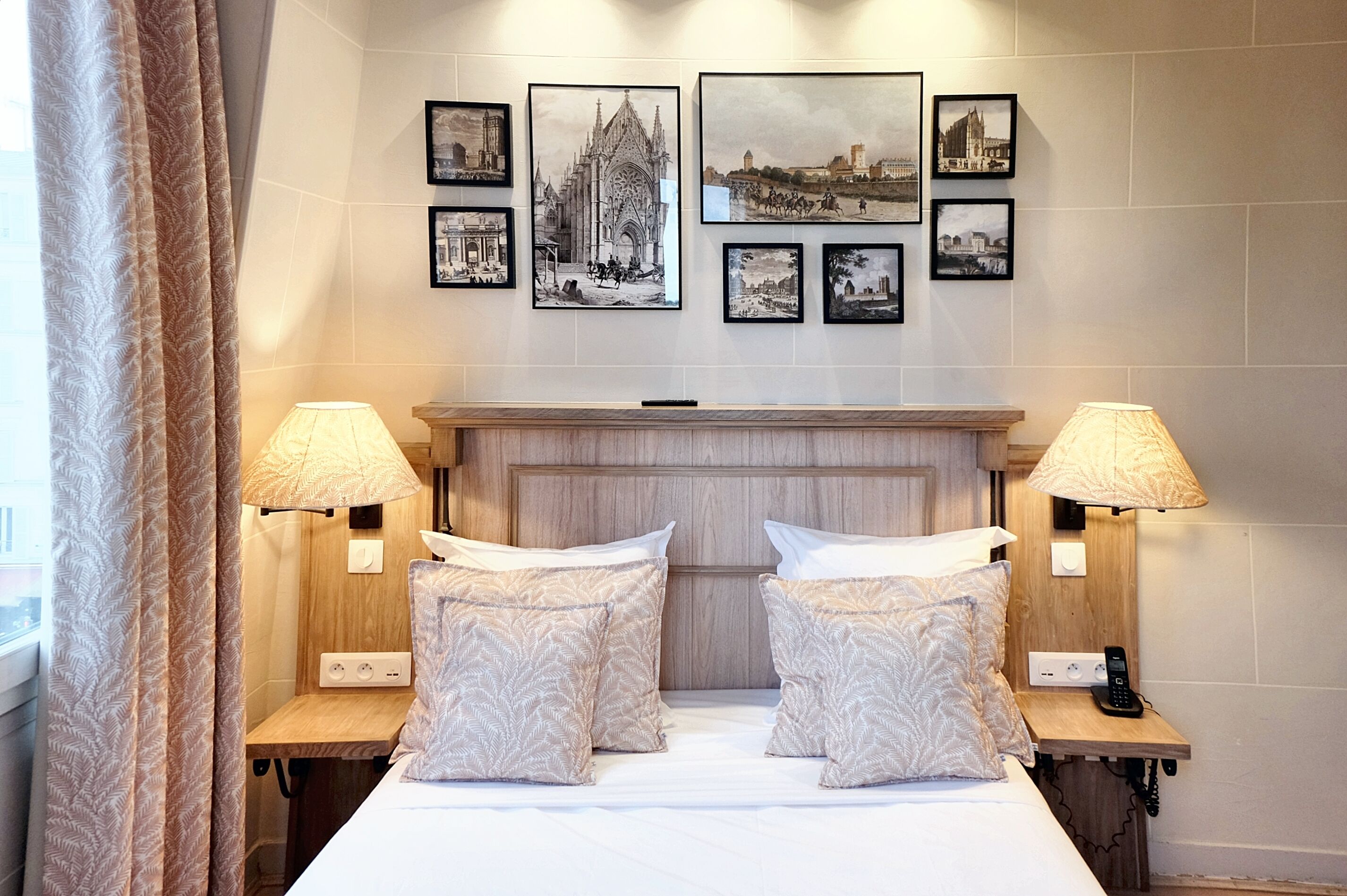 A hotel room with a bed, two bedside tables, lamps, a wooden headboard, and framed pictures on the wall.