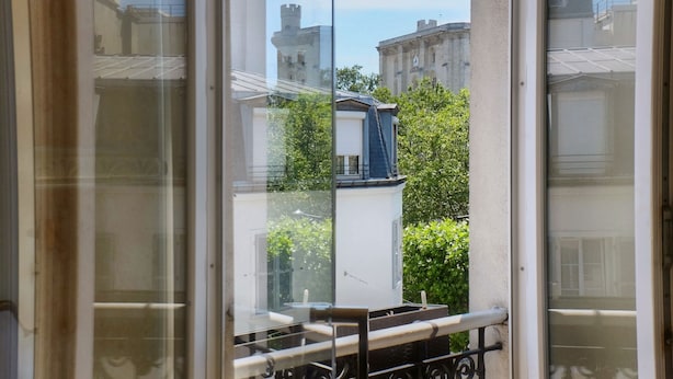 Ein Balkon mit Glastür, Metallgeländer und Blick auf Gebäude und Grünflächen.