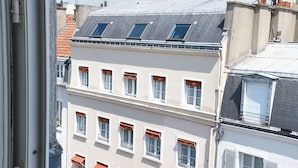 Blick auf ein Gebäude mit mehreren Fenstern und Balkonen, aufgenommen durch ein Fenster mit weißem Rahmen.