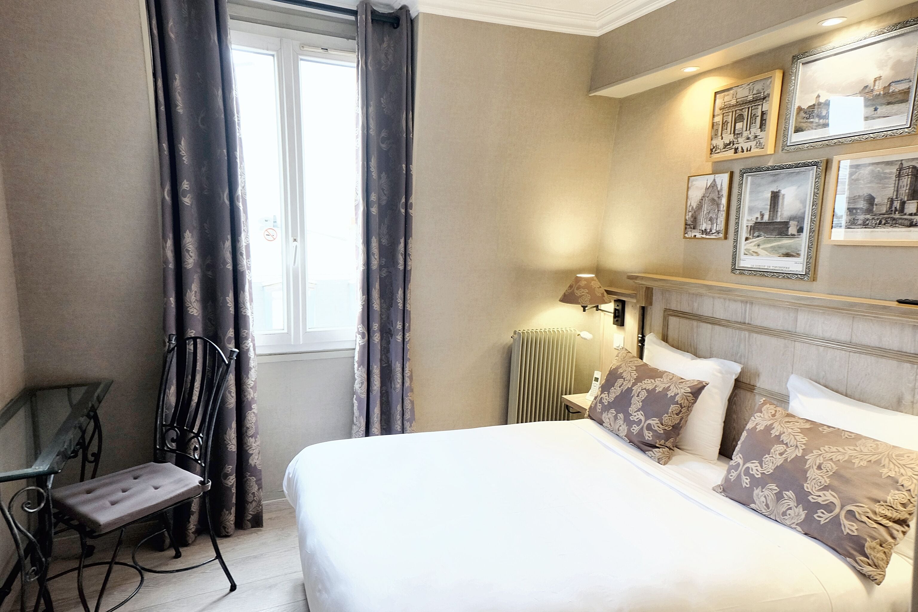 A hotel room with a large bed, a desk, a chair, and a window with curtains.