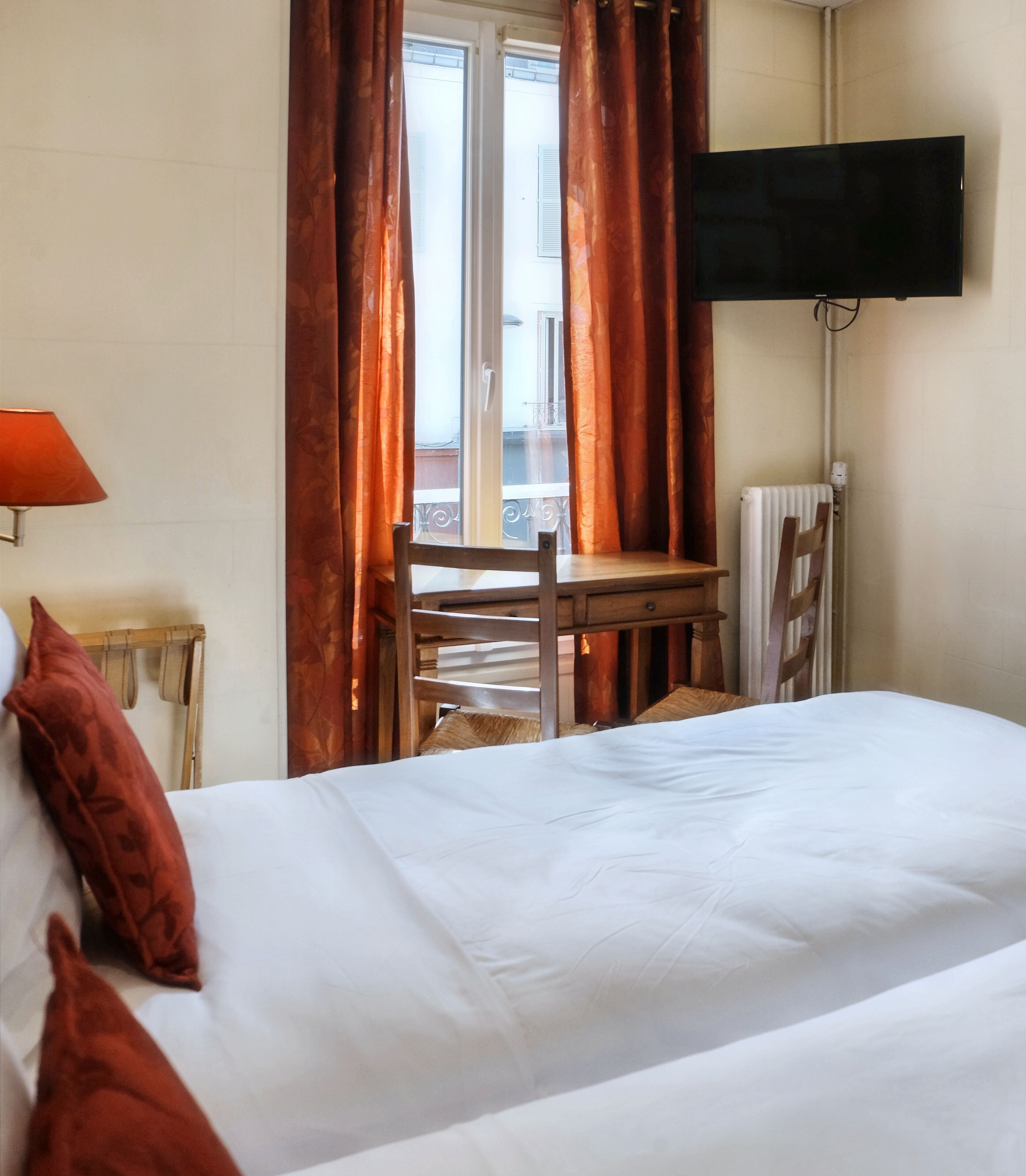 A hotel room with a bed, a desk, a chair, a TV, and a window with curtains.