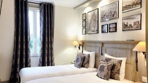 Ein Hotelzimmer mit zwei Betten, einem Fenster mit Vorhängen, Wandlampen und gerahmten Bildern an der Wand.