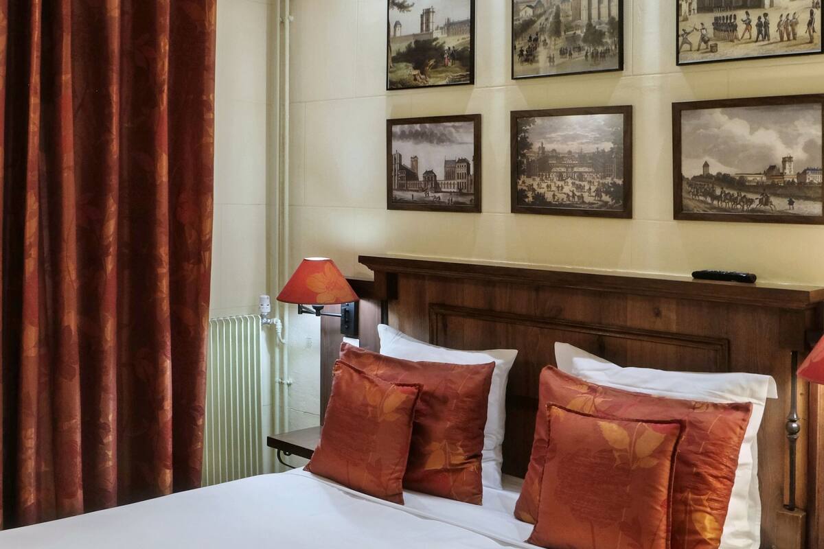 A hotel room with a large bed, red curtains, and multiple framed pictures on the wall.
