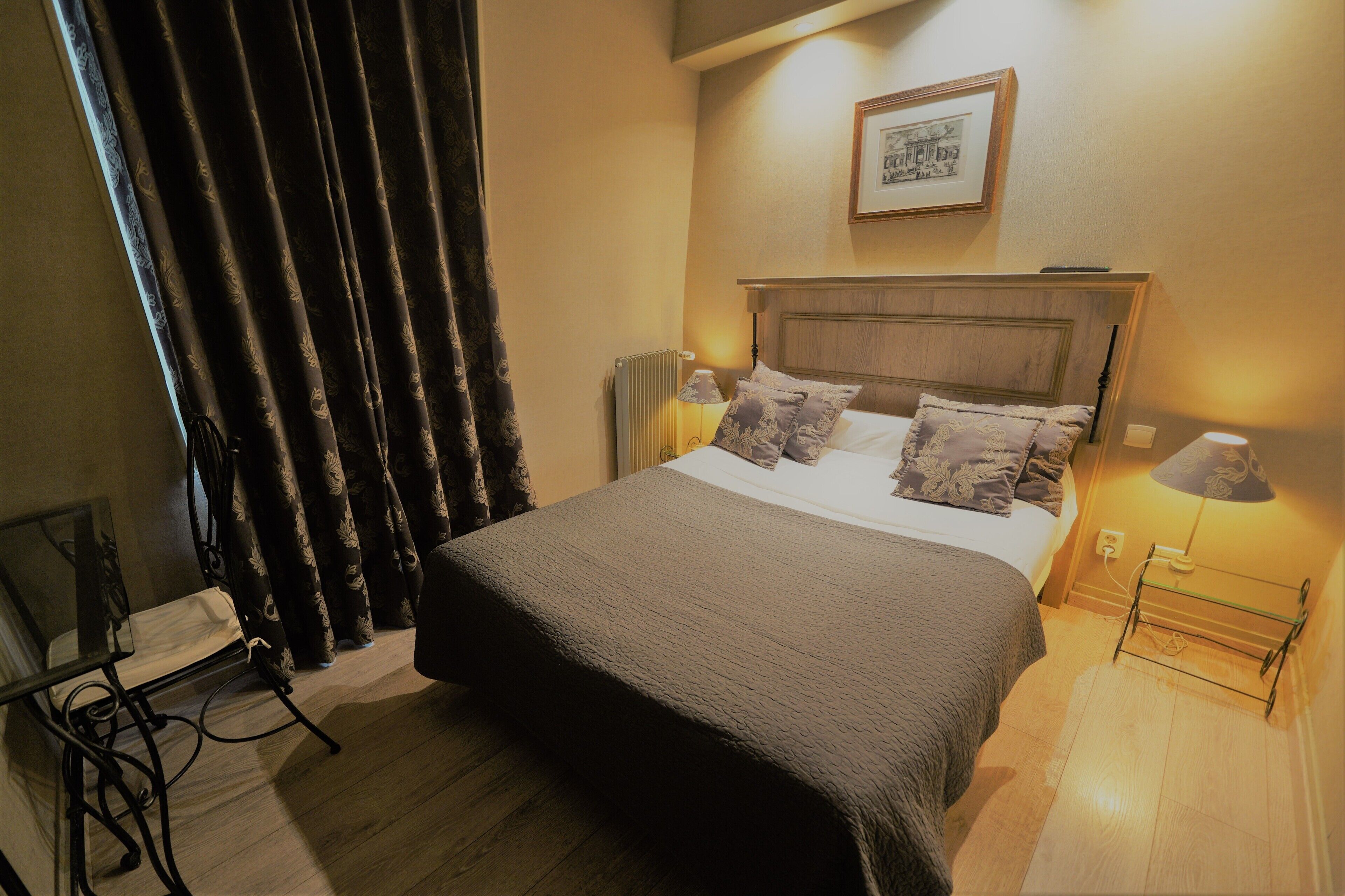 A neatly made bed with a headboard, two bedside lamps, and a framed picture on the wall.