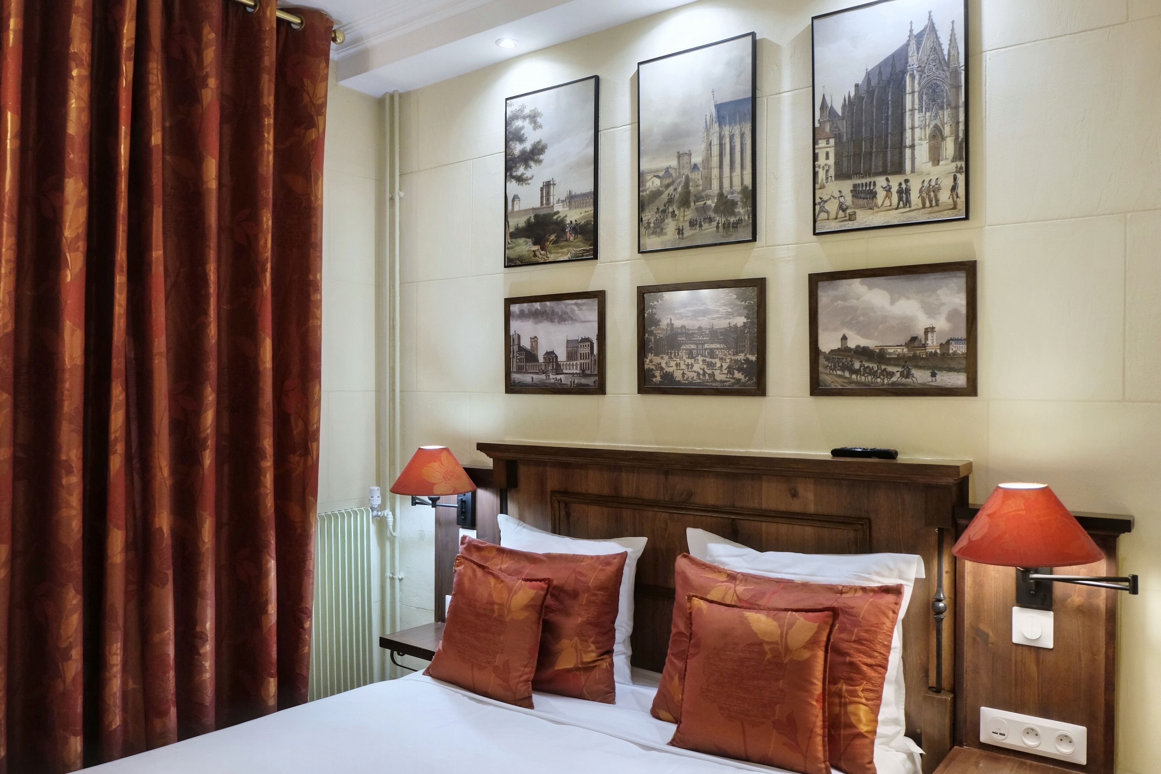 A hotel room with a wooden headboard, a bed with white bedding and brown patterned pillows, two bedside lamps, and four framed pictures on the wall.