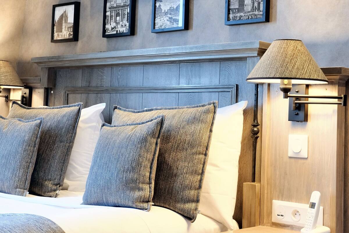 A hotel room with a bed, bedside lamps, a mounted phone, and framed pictures on the wall.