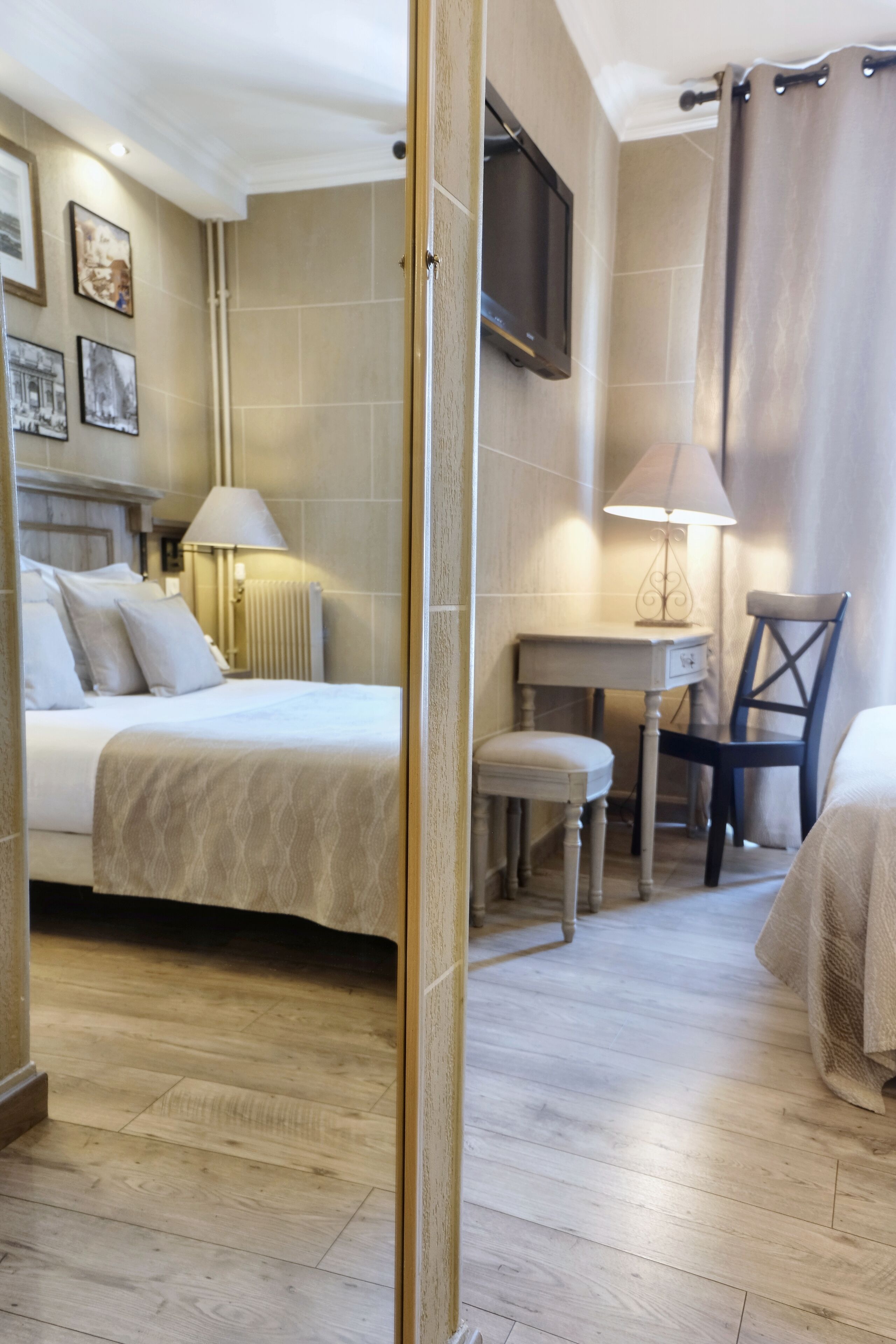 A hotel room with two beds, a desk, a chair, a lamp, and a television on the wall.