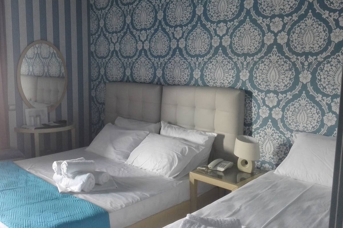 Ein Hotelzimmer mit einem Bett, einem Nachttisch mit Lampe, einem Spiegel und einer Wand mit Muster.
