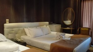 A hotel room with a large bed, a bedside table with a lamp, a mirror, a chair, and a small table with towels.