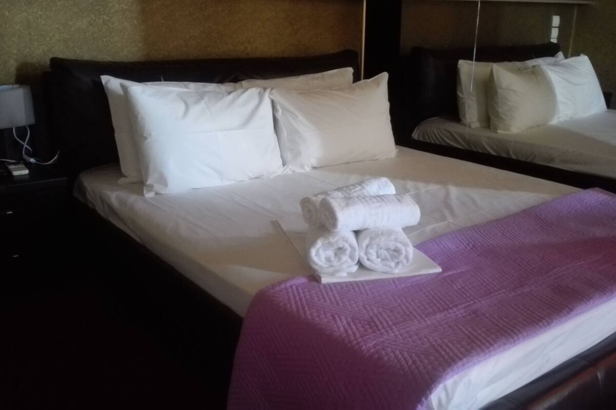 Ein Hotelzimmer mit einem großen Bett, zwei Kissen, einem Nachttisch mit einer Lampe und einer violetten Decke.
