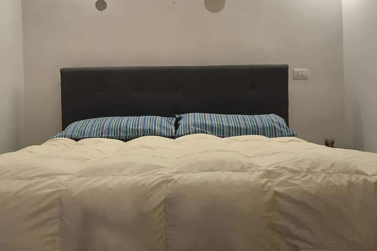 A bed with a dark headboard, two striped pillows, and a cream-colored duvet.