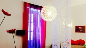 A room with a bed, a TV, a red chair, a small table, and a decorative light fixture. - Agriturismo Belvedere (Piano di Sorrento)