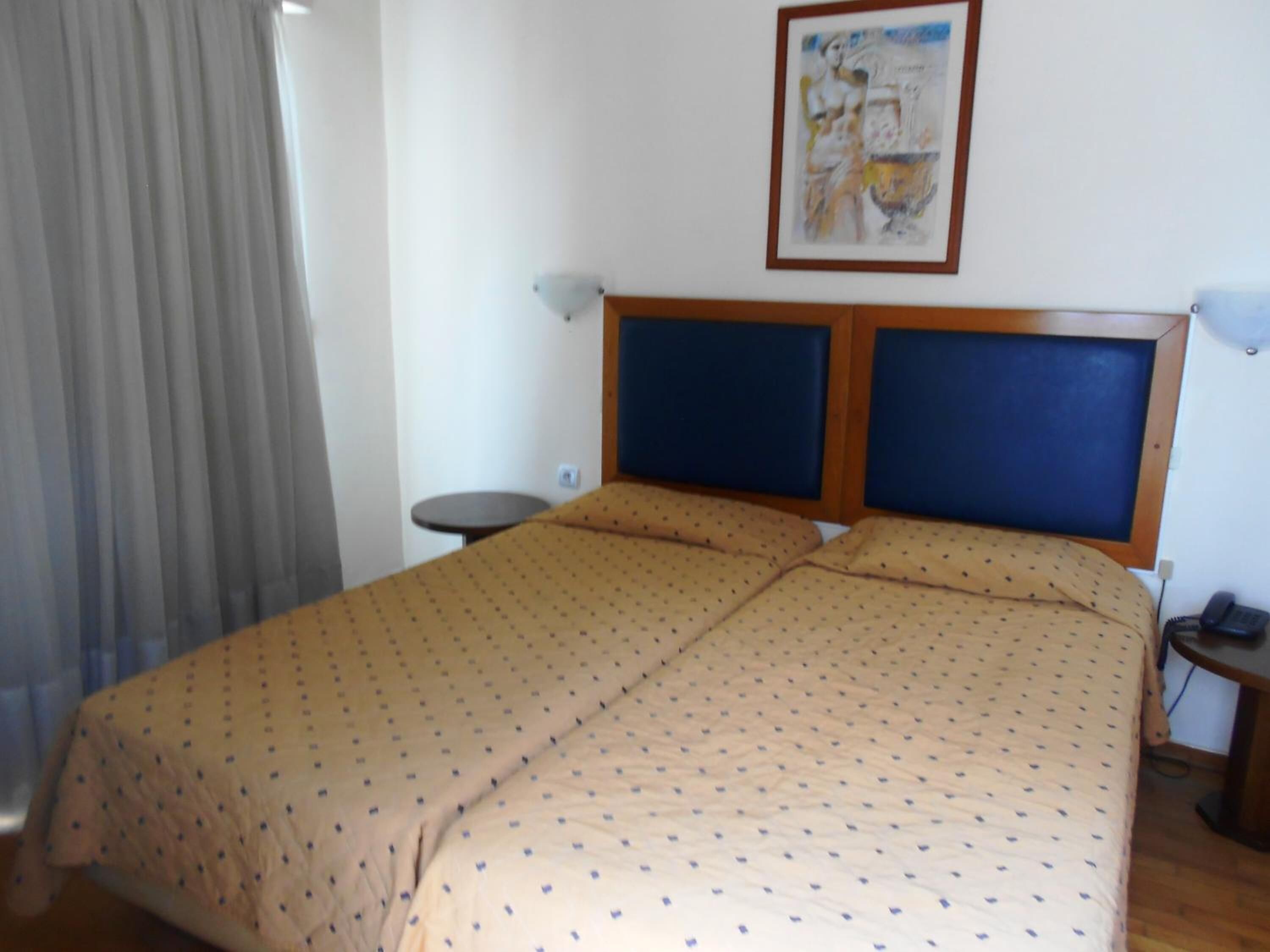 Ein Hotelzimmer mit einem großen Bett, einem kleinen runden Tisch, einem Telefon und einem Gemälde an der Wand.