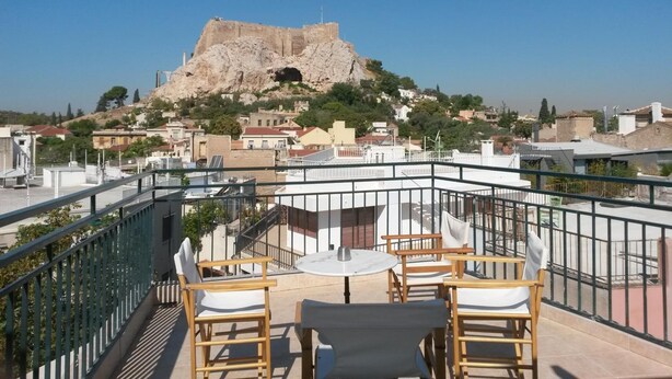 Terraza en la azotea con una mesa y sillas, con vistas a una colina rocosa con la entrada de una cueva.