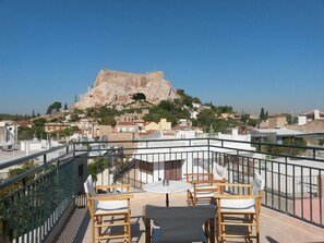 A rooftop terrace with a table and chairs, overlooking a rocky hill with a cave entrance. - Adams Hotel (Athens)