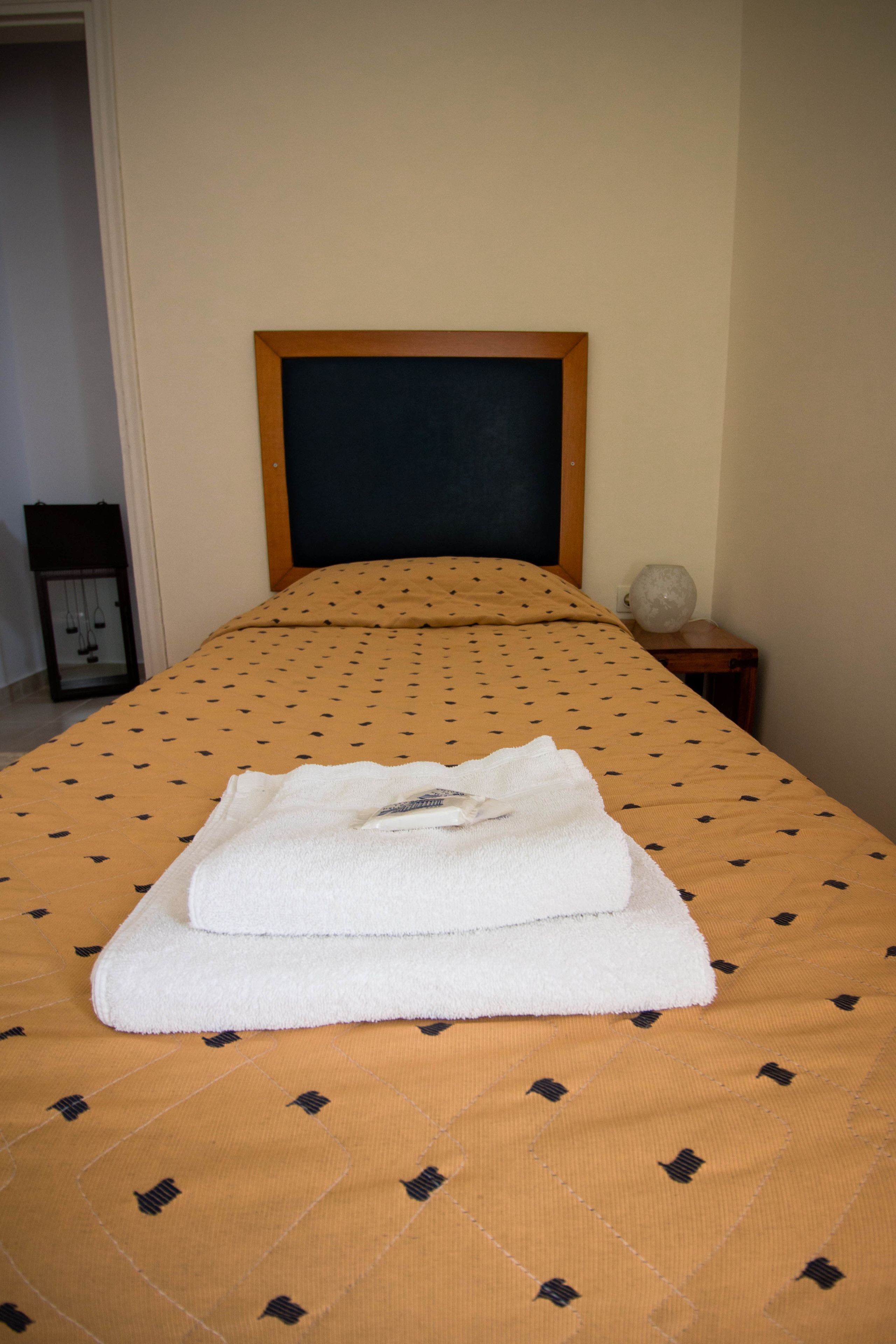 A neatly made bed with a patterned bedspread and a folded white towel on top.