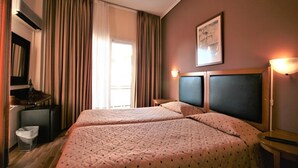 Habitación de hotel con dos camas, un escritorio, una silla y una ventana con cortinas.