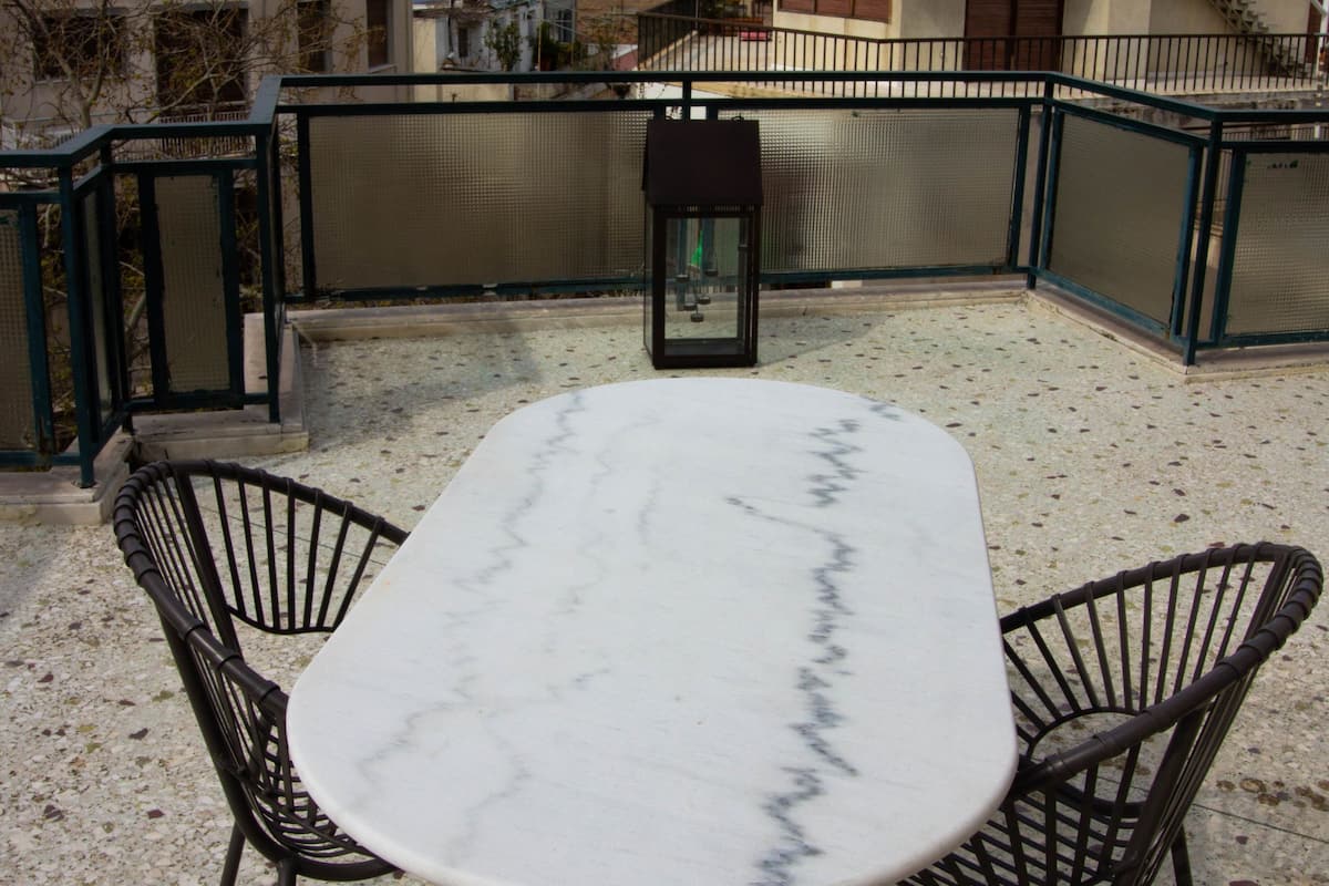 Una terraza en la azotea con una mesa de mármol y dos sillas, con vistas a una fortaleza histórica y edificios circundantes.