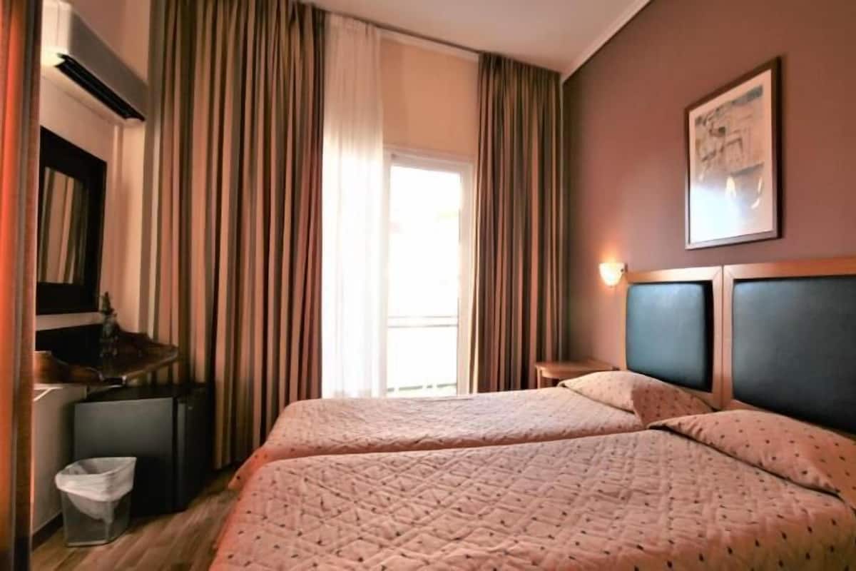 Habitación de hotel con dos camas, un escritorio, una silla, un cesto de basura y una ventana con cortinas.