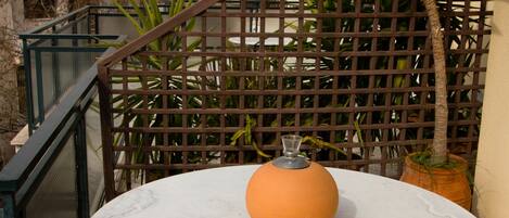 A round table with a vase, surrounded by metal chairs, set on a balcony with a view of a historic building and a rocky hill.