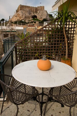A round table with a vase, surrounded by metal chairs, set on a balcony with a view of a historic building and a rocky hill. - Adams Hotel (Athens)
