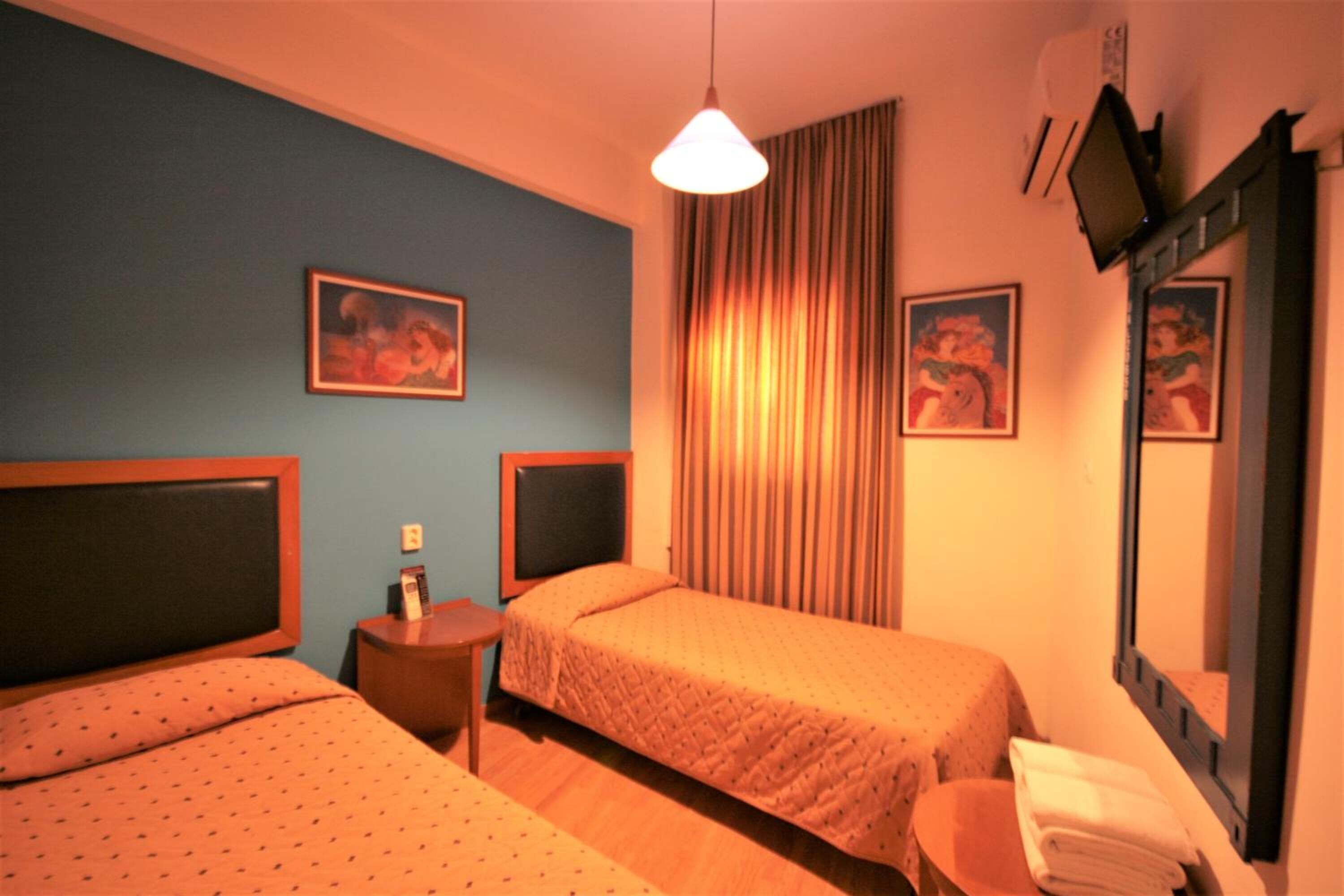 Una habitación de hotel con dos camas, una mesita, un espejo y dos cuadros en la pared.