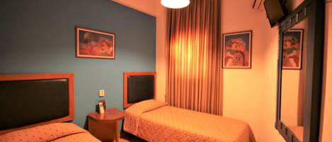 Une chambre d’hôtel avec deux lits, une petite table, un miroir et deux tableaux accrochés au mur.