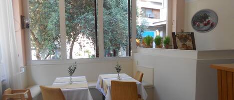 A dining area with two tables, four chairs, and a view of trees through arched windows.