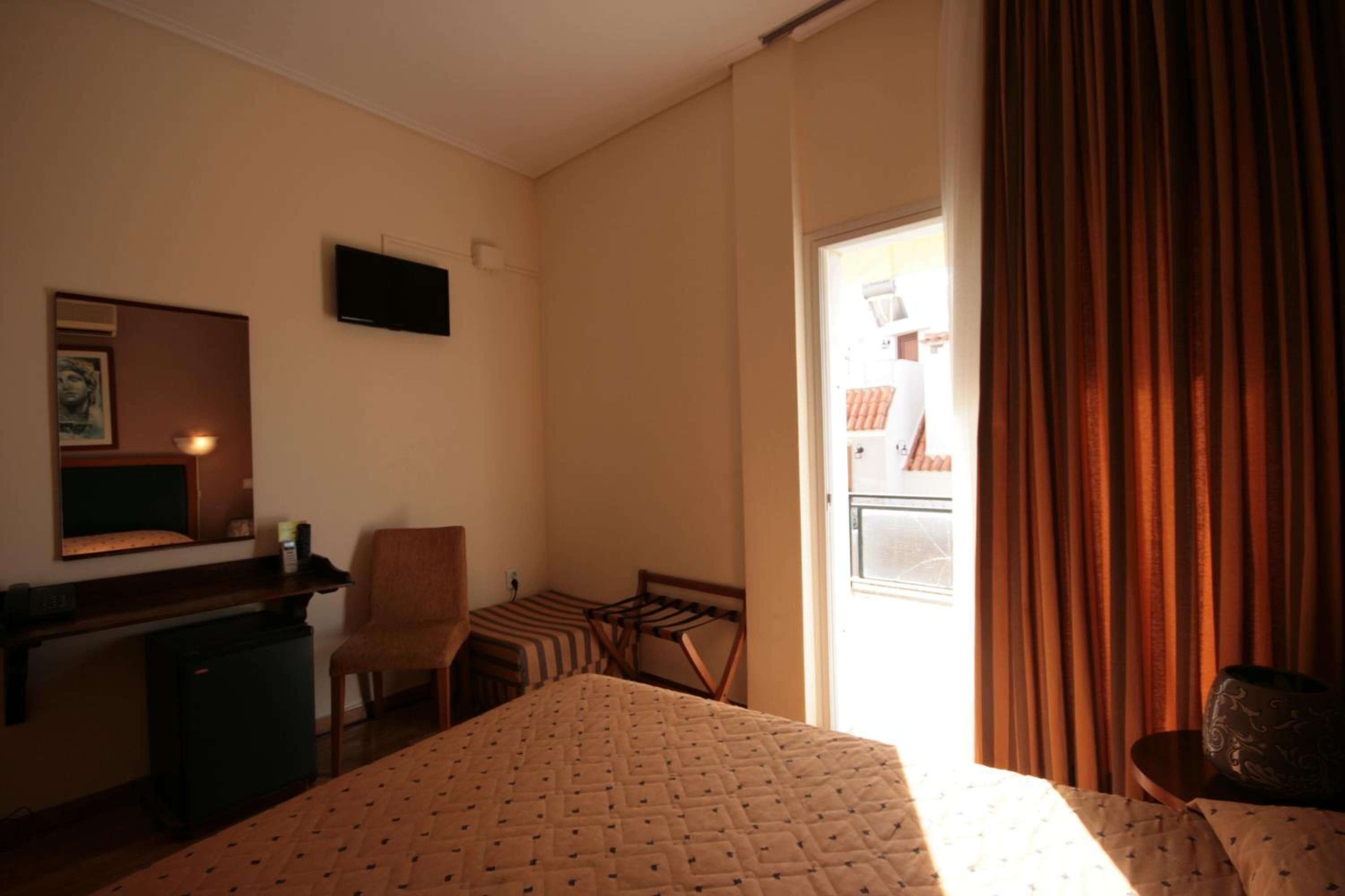 A hotel room with a bed, a desk, a chair, a television, and a window with curtains.