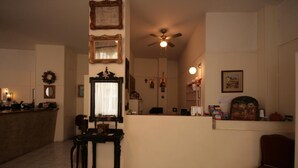 Una sala de estar acogedora con una mesa de madera, un ventilador de techo y una zona de cocina con mostrador y varios objetos.