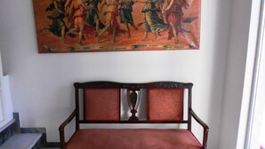 Una habitación con un banco de madera y un cuadro clásico grande en la pared.