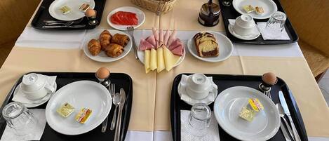 A breakfast setting with two tables, each with a tray containing croissants, ham, cheese, and a small dish of jam.