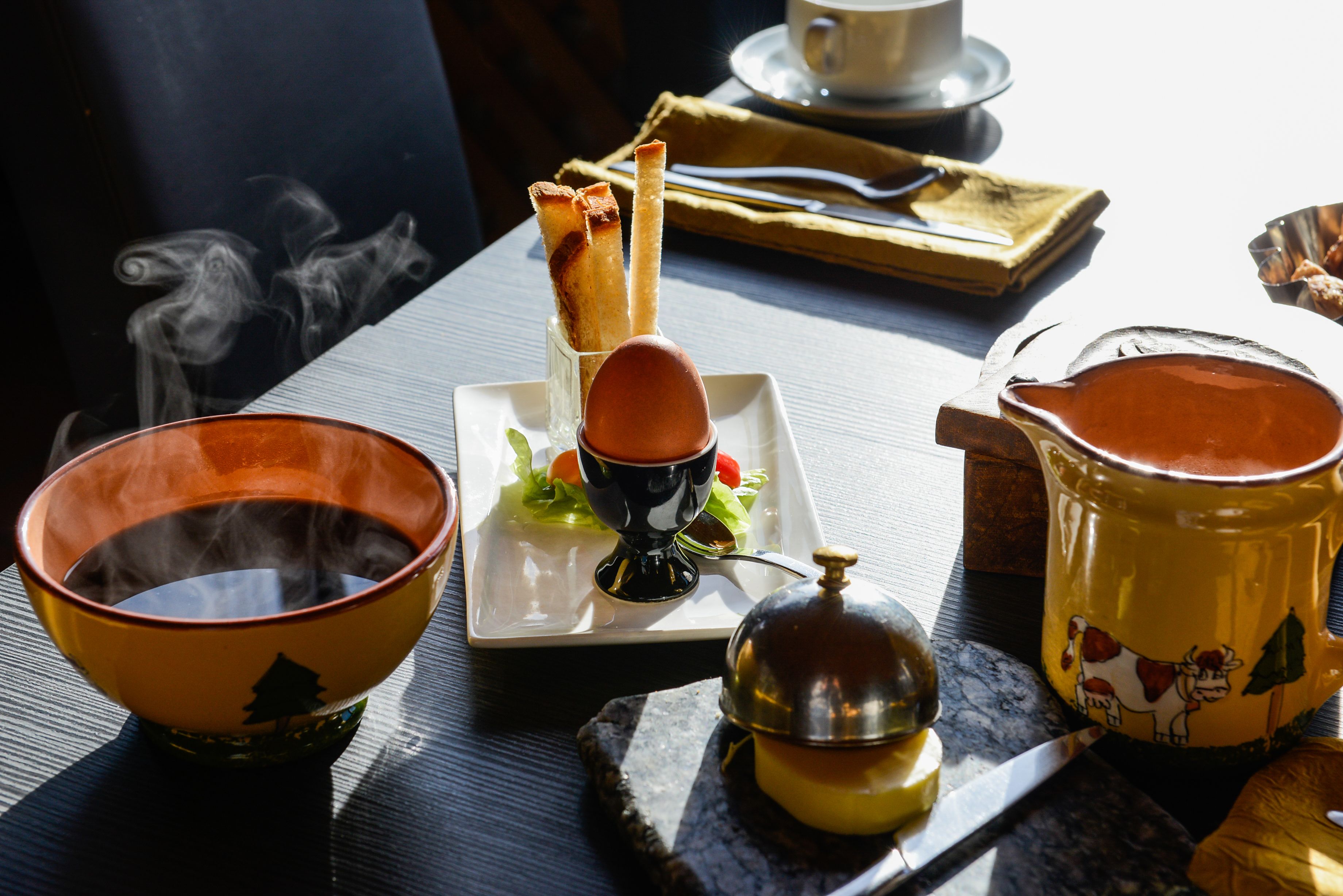 A table set with a teapot, a cup, a bowl, and a plate with food.