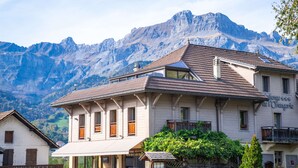 A two-story building with a traditional Alpine architectural style, featuring a sloped roof and wooden shutters. In the background, there are mountains and a clear sky. - Best Western Plus Pays du Mont Blanc (Passy)