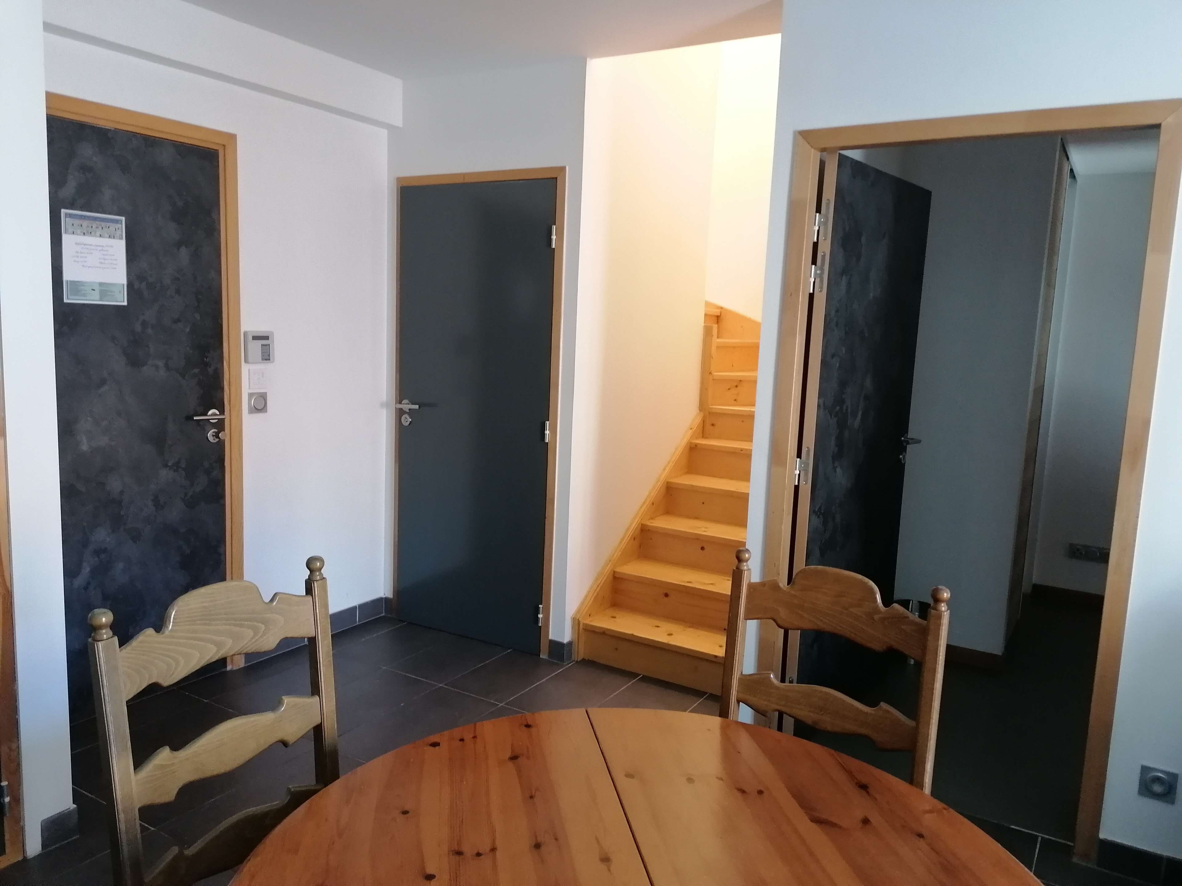 A room with a wooden dining table and chairs, a staircase, and a door with a light switch.