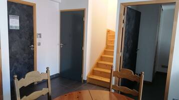 A room with a wooden dining table and chairs, a staircase, and a door with a light switch.